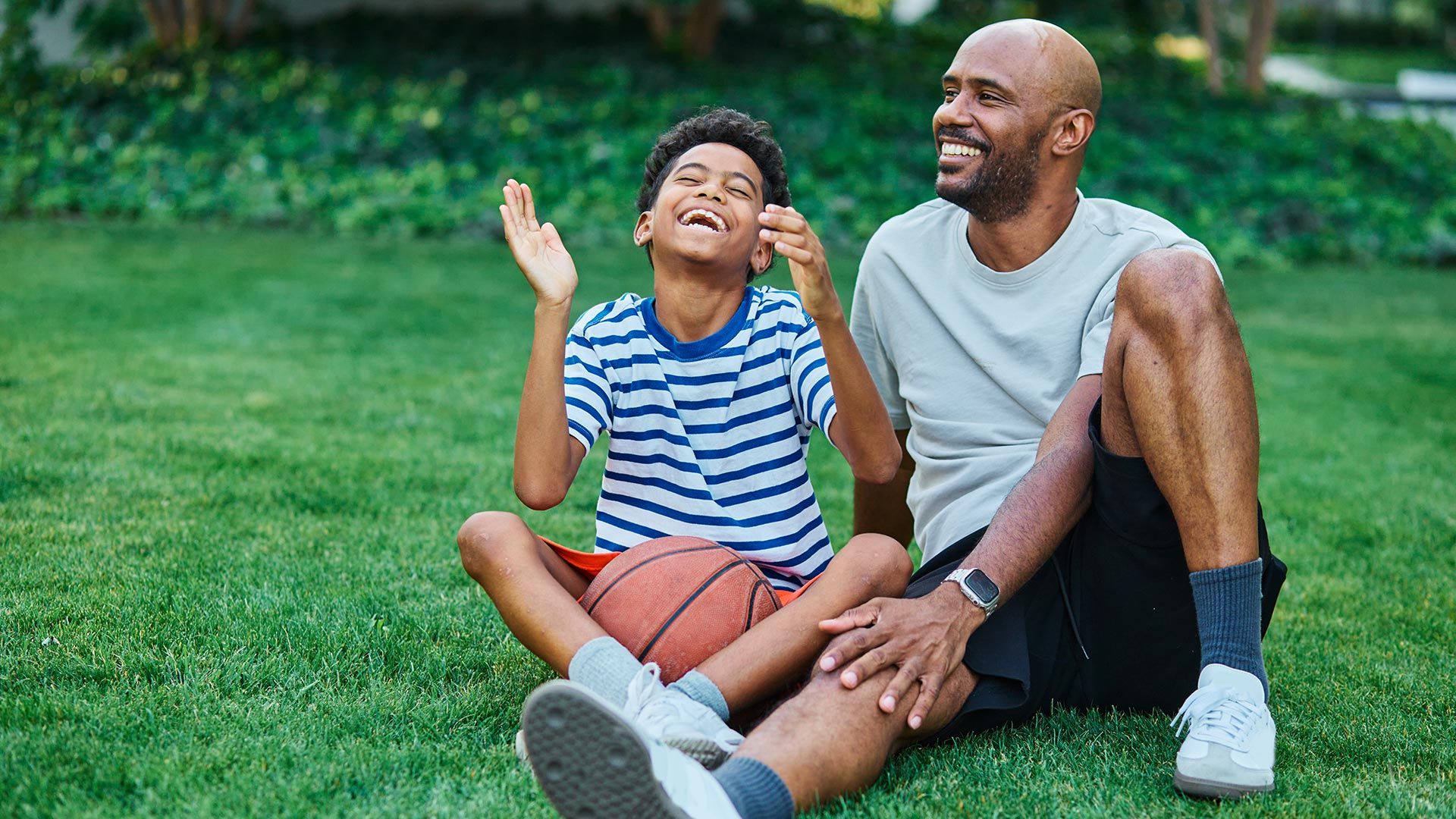 Father and son sit in the grass with a basketball