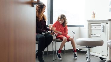 A mother and her daughter wearing an arm cast wait in a medical office