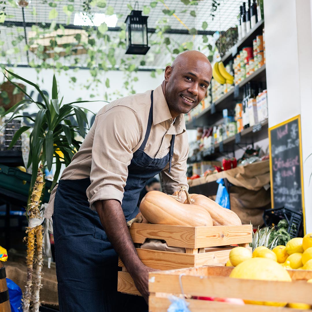 Grocery store worker bends over to pick up a crate of produce