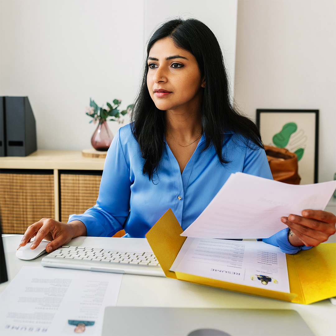 Woman holding papers working on her computer