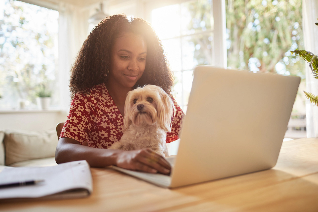 woman holding her dog while also working on a laptop at home