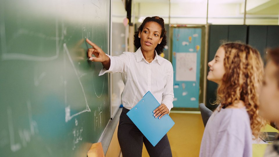 Teacher at blackboard helping students solve math problem