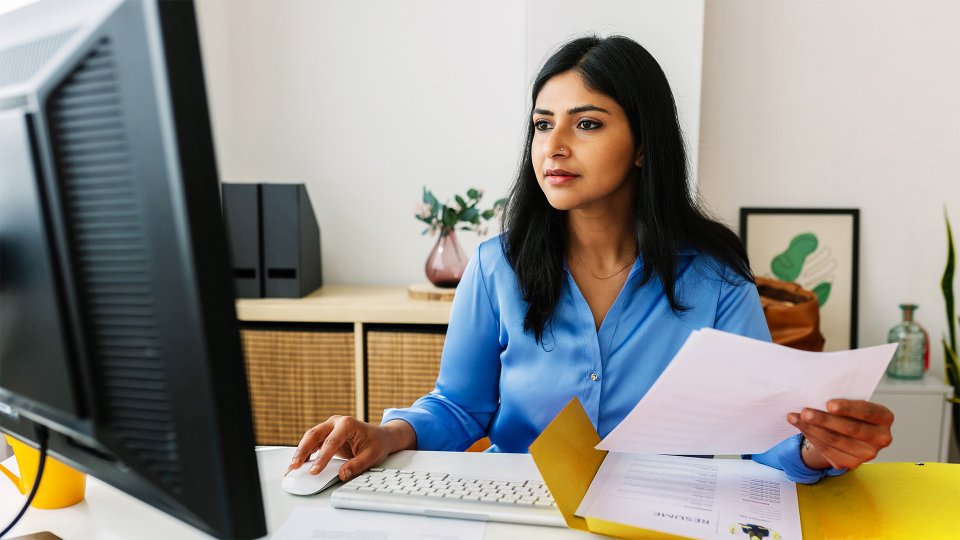 Woman holding papers working on her computer