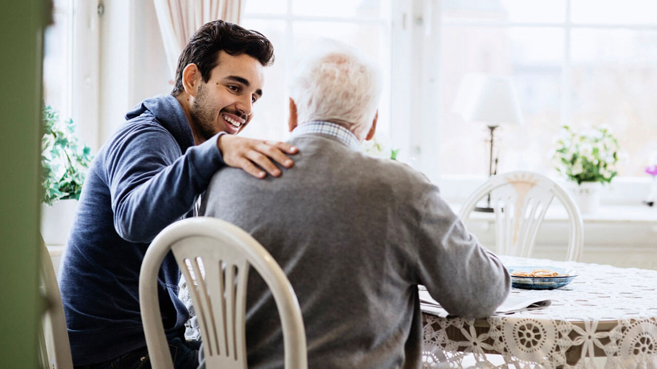 Father & son sitting in a kitchen and Son caring for their elderly parent
