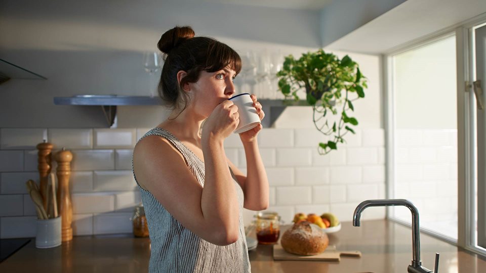 Woman sipping coffee in her kitchen in the early morning light