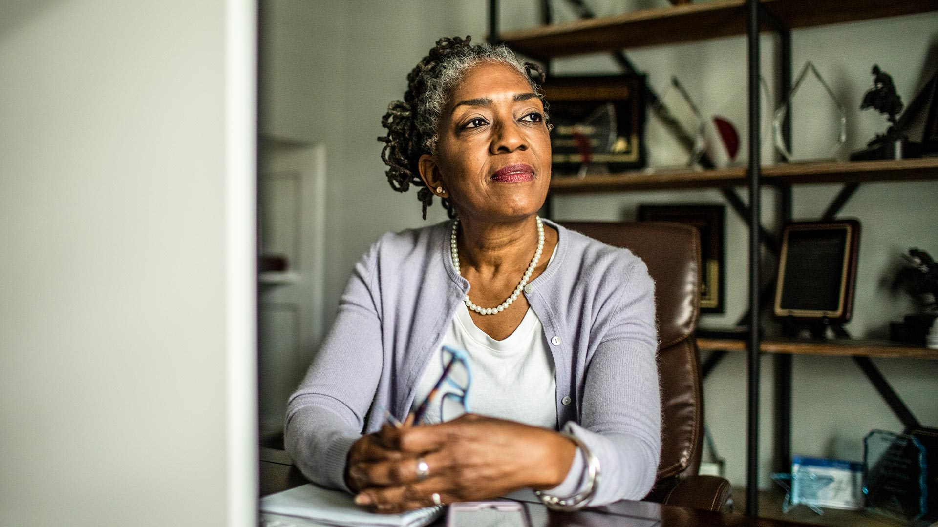 Retirement age woman sitting at desk looks thoughtful